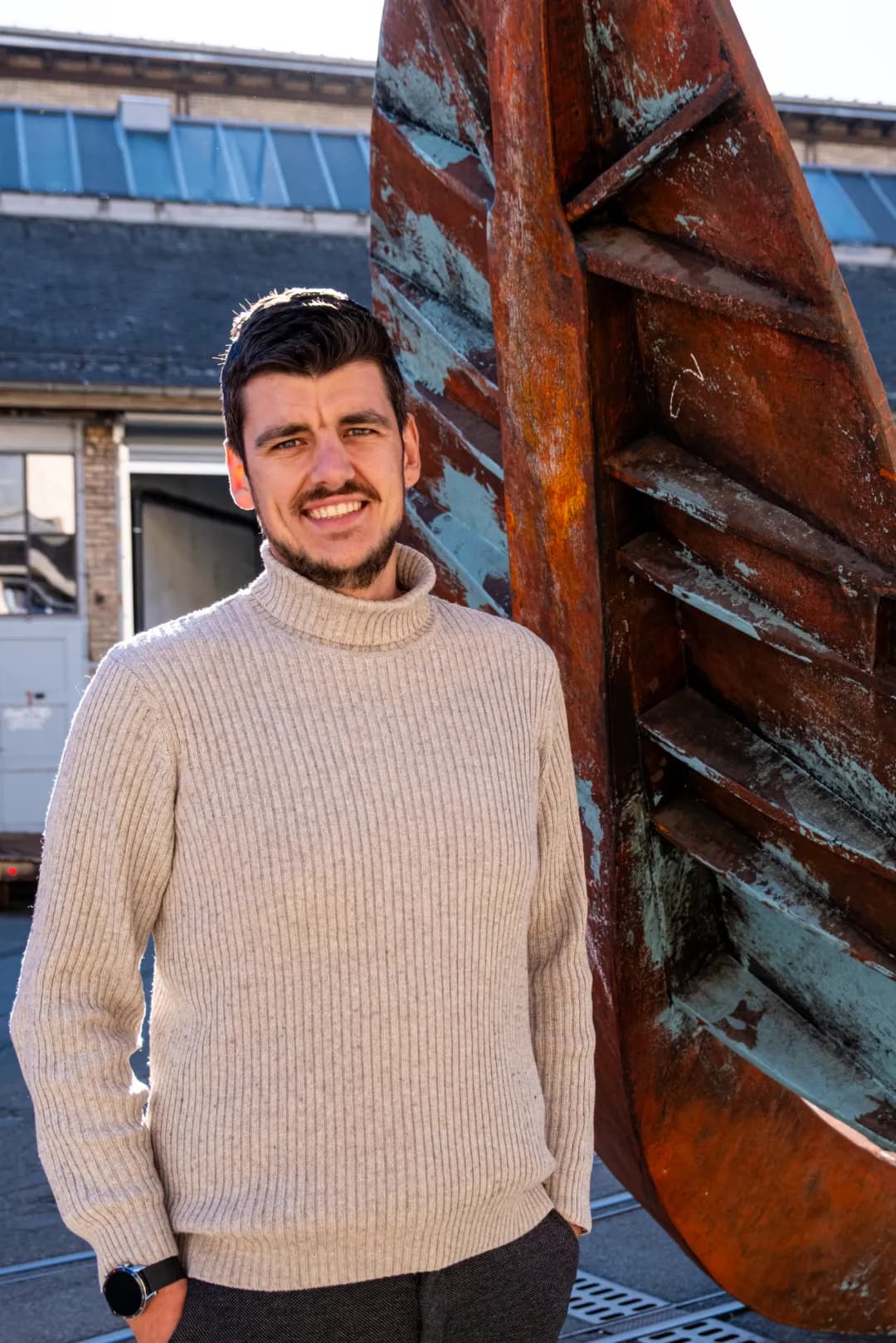 Nicolas Fischer, im urbanen Bereich vor einem rostigen Anker stehend